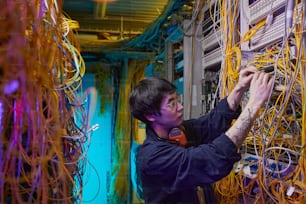 Vista laterale ritratto del giovane tecnico di rete che collega fili e cavi nella sala server, spazio di copia