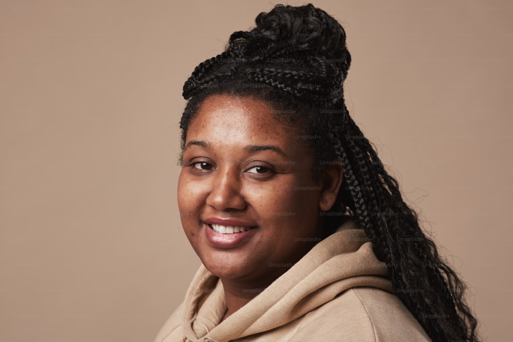 Minimal close up portrait of curvy African American woman smiling at camera while posing against neutral beige background in studio, copy space