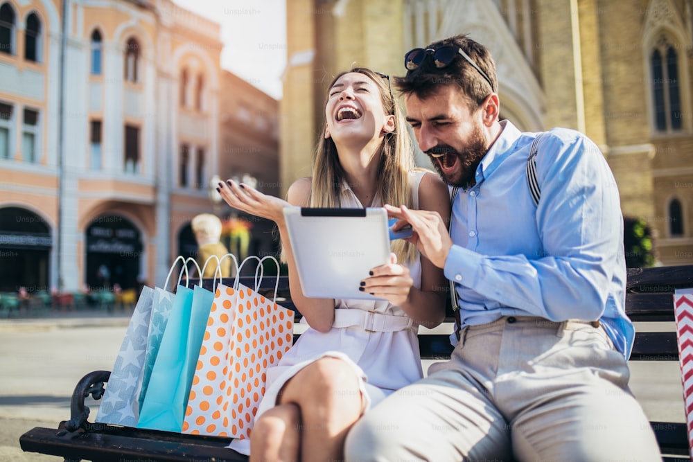 Jeune couple utilisant une tablette numérique pour faire des achats en ligne en plein air.