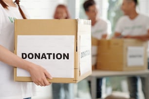 Cropped image of female volunteer holding cardboard box of donated clothes and groceries