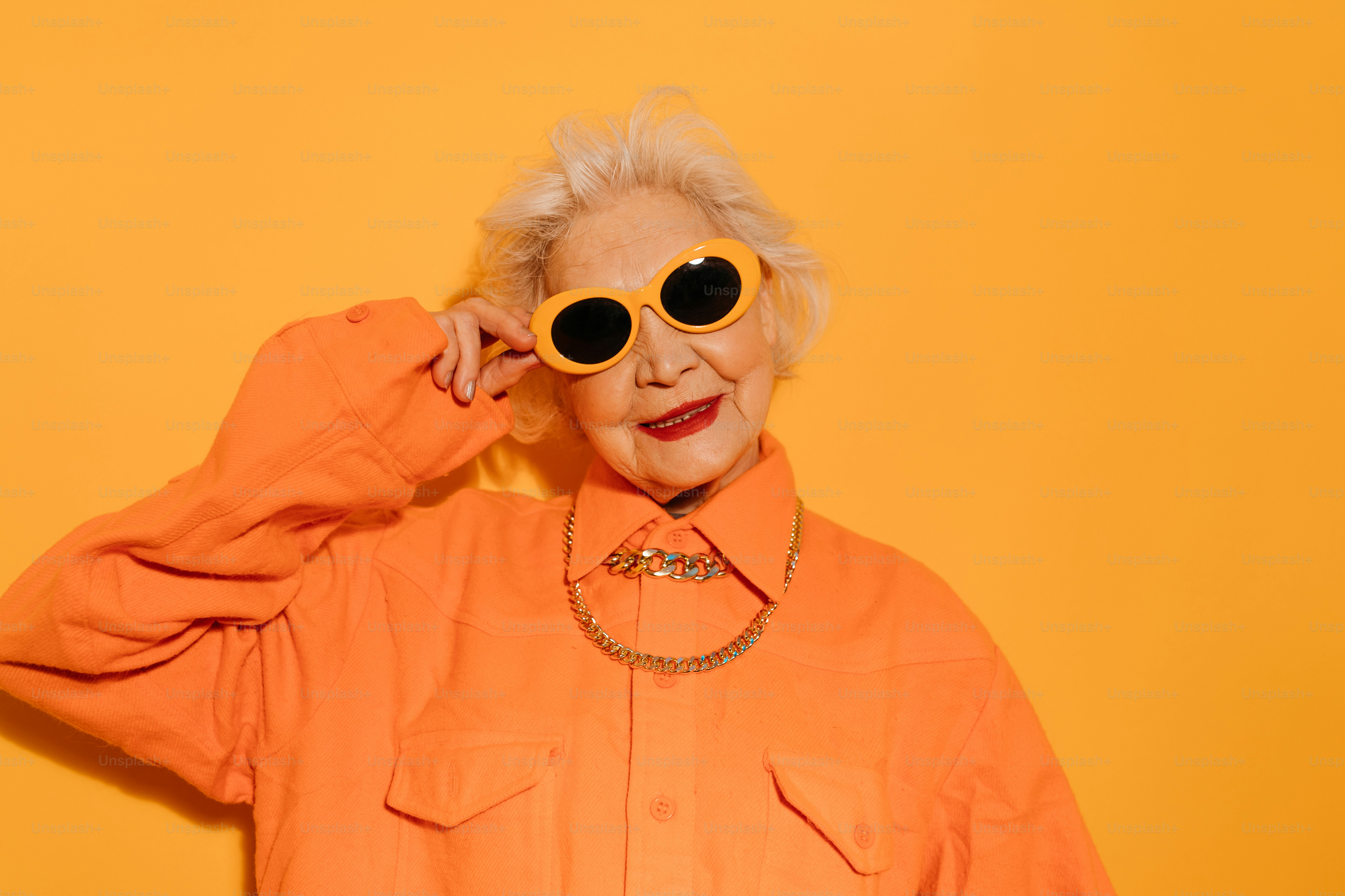 An older woman in an orange shirt wearing yellow sunglasses and gold chains