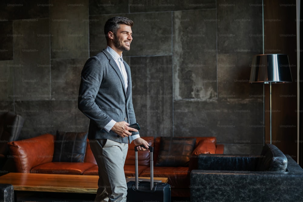 A male businessman dressed elegantly carries luggage and a mobile phone in the hotel lobby. He's on a business trip. Travel, symposium, ready to go