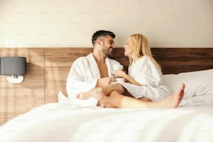 We celebrate love, gentle touches in bed with coffee. Romantic moments to remember, a middle-aged happy loving couple in a hotel bathrobe talking and laughing. Love, lifestyle, emotional, feelings