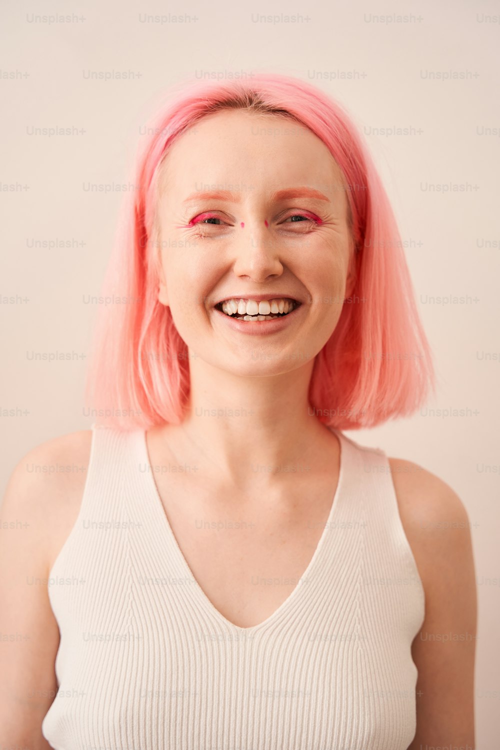 Vista ritratto della donna sorridente e allegra con i capelli rosa e il trucco vivido che ride mentre posa davanti alla fotocamera. Immagine