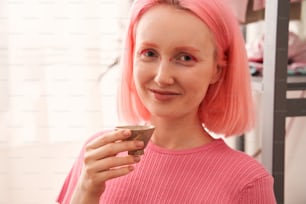Portrait view of the woman with pink hair and vivid makeup looking at the camera and enjoying of the traditional japanese tea at her morning ceremony. Stock photo
