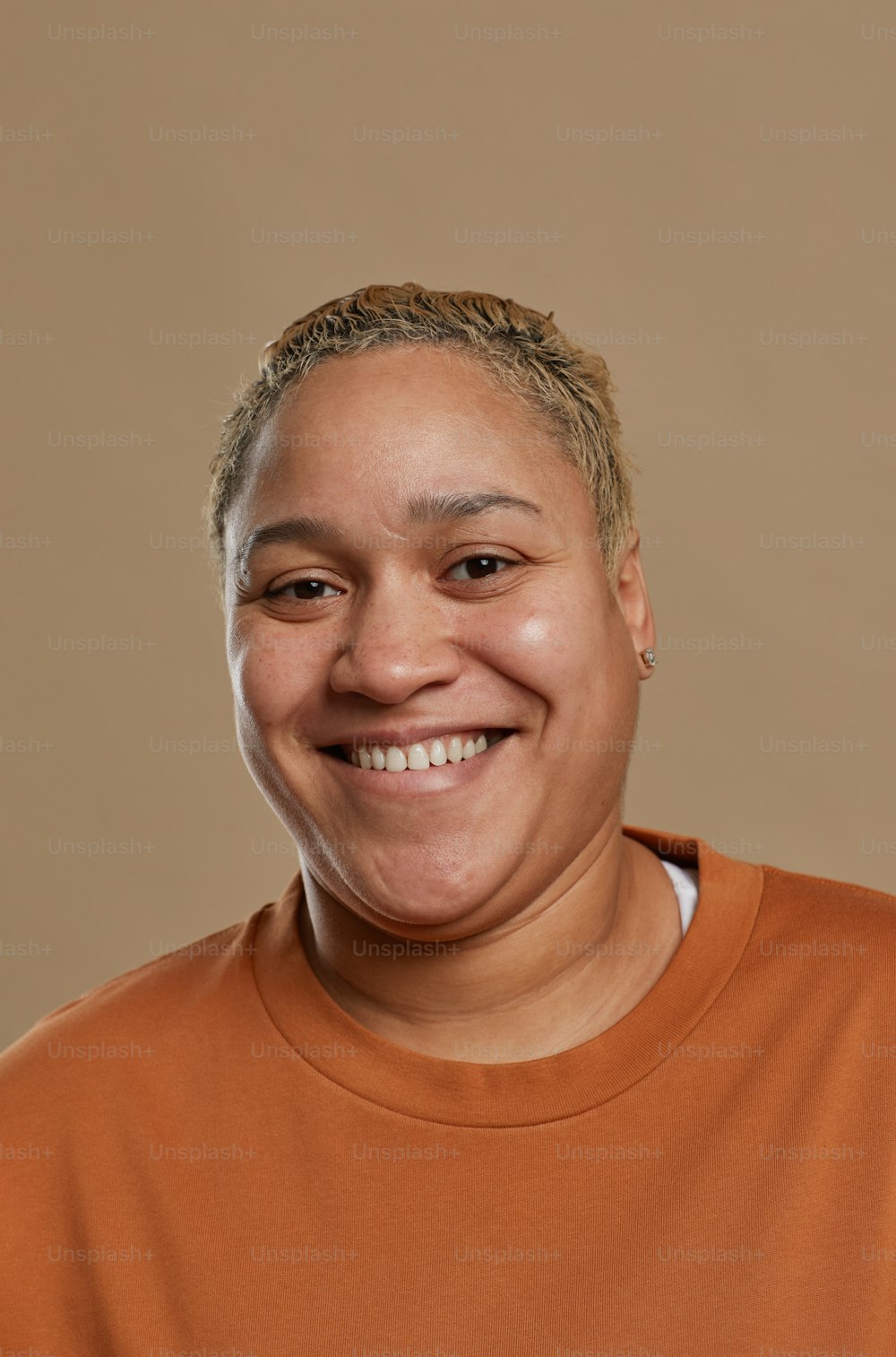 Retrato vertical de una mujer de raza mixta de pelo corto mirando a la cámara y sonriendo felizmente mientras posa contra un fondo neutral en el estudio