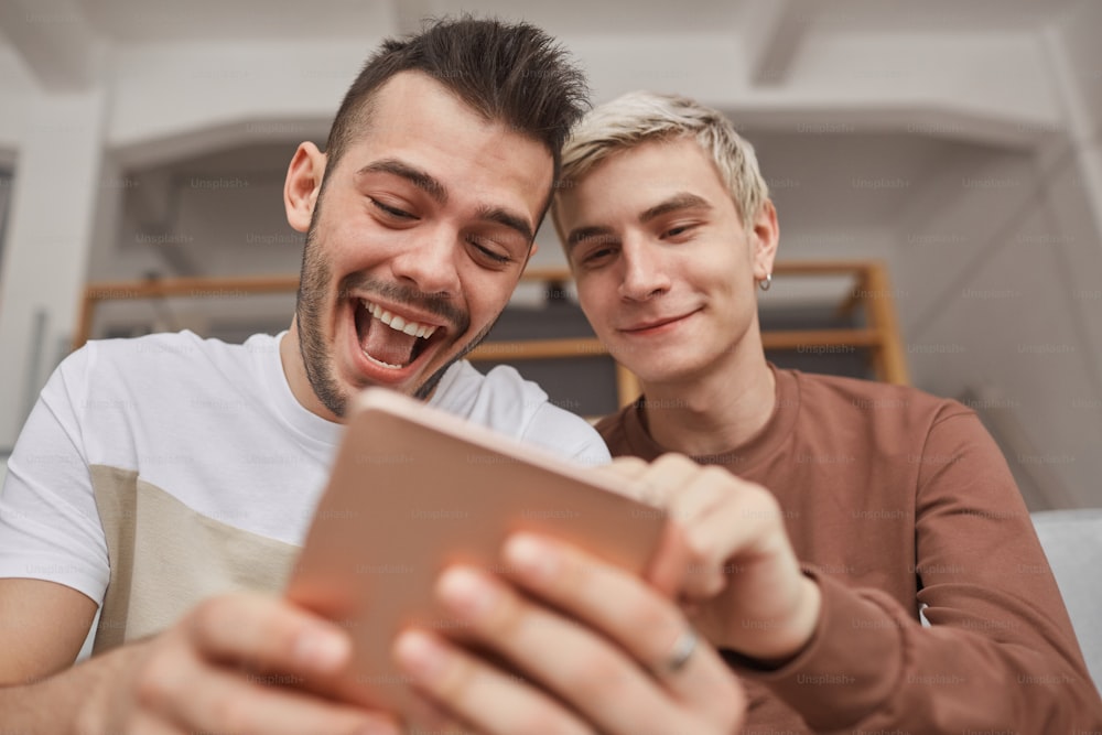 Low angle portrait of two young men laughing while looking at tablet screen in home interior