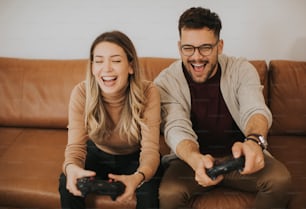 Handsome young couple playing video games at home, sitting on sofa and enjoying themselves