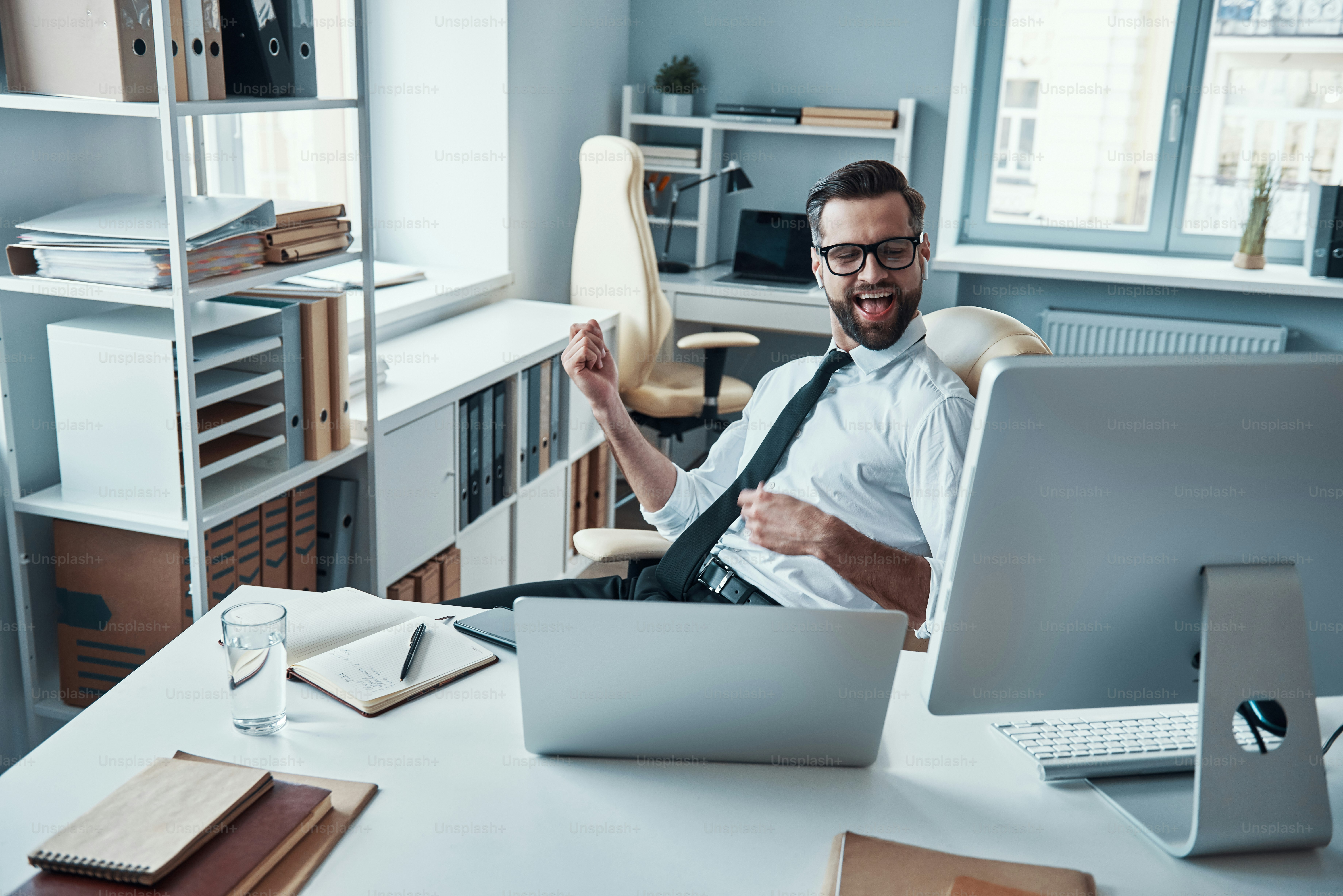 Happy young man in shirt and tie relaxing by listening music while sitting in the office