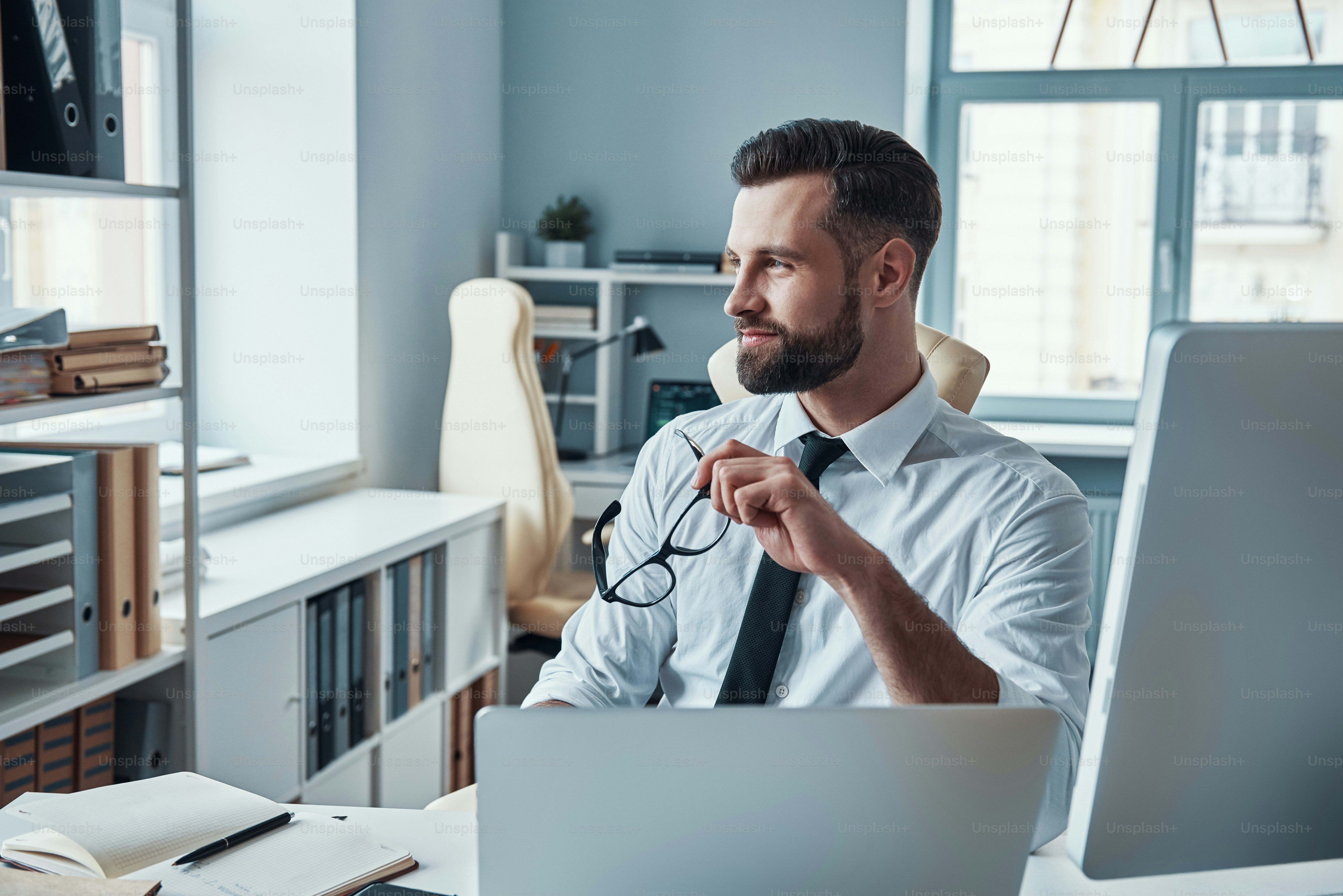 Thoughtful young man in formalwear looking away and smiling while sitting in the office