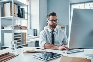 Modern young man in formalwear working using technologies while sitting in the office