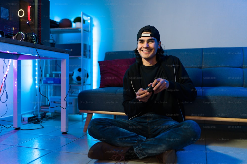 興奮した若い男性が笑顔で、寝室の床にリモコンでアクションビデオゲームをプレイしている