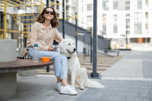 Cheerful woman sitting on bench with big white dog in the courtyard of the residence. Animal lover, pet friendly owner.
