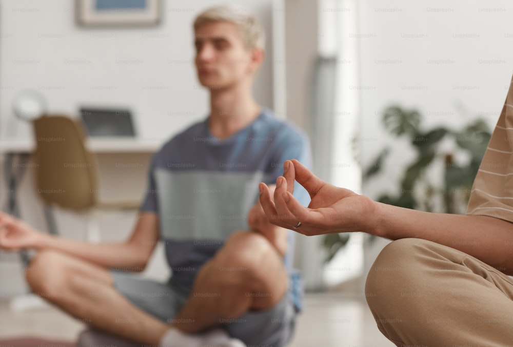 Close up of two young men meditating at home while enjoying yoga exercises sitting on mats in lotus position, copy space