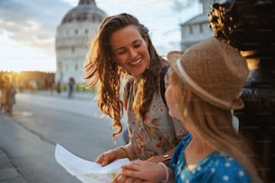 ピサ大聖堂近くの地図を持つ笑顔のトレンディな母と娘。