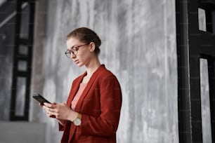 Portrait of young businesswoman wearing red while standing against grey wall in office, copy space