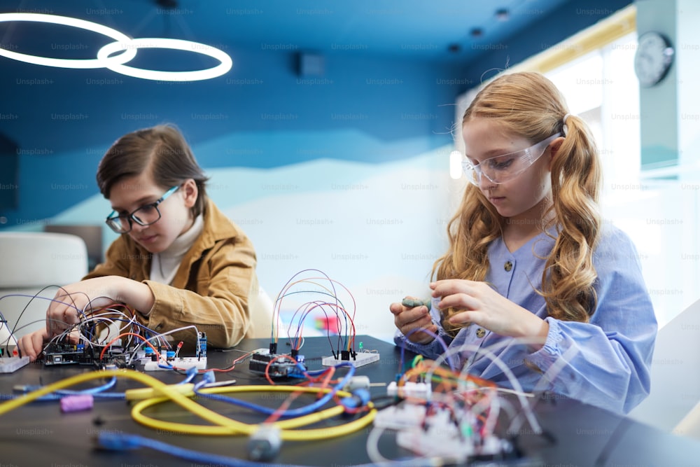 Portrait of two kids building robots and experimenting with electric circuits in engineering class at school