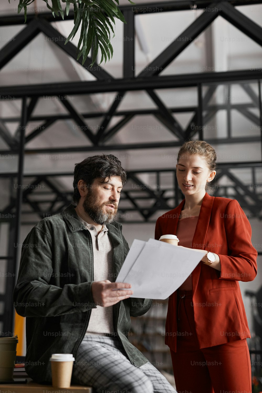 Vertical portrait of contemporary bearded businessman talking to female colleague and holding documents in graphic office interior