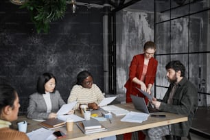 Il team aziendale diversificato discute il progetto in interni dell'ufficio nero si concentra sulla giovane donna d'affari che indossa la giacca rossa, lo spazio di copia