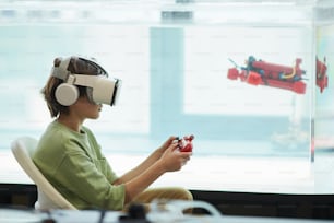 Seitenansichtsporträt eines Jungen, der VR-Headset trägt, während er ein Roboterboot im Schullabor bedient, Kopierraum