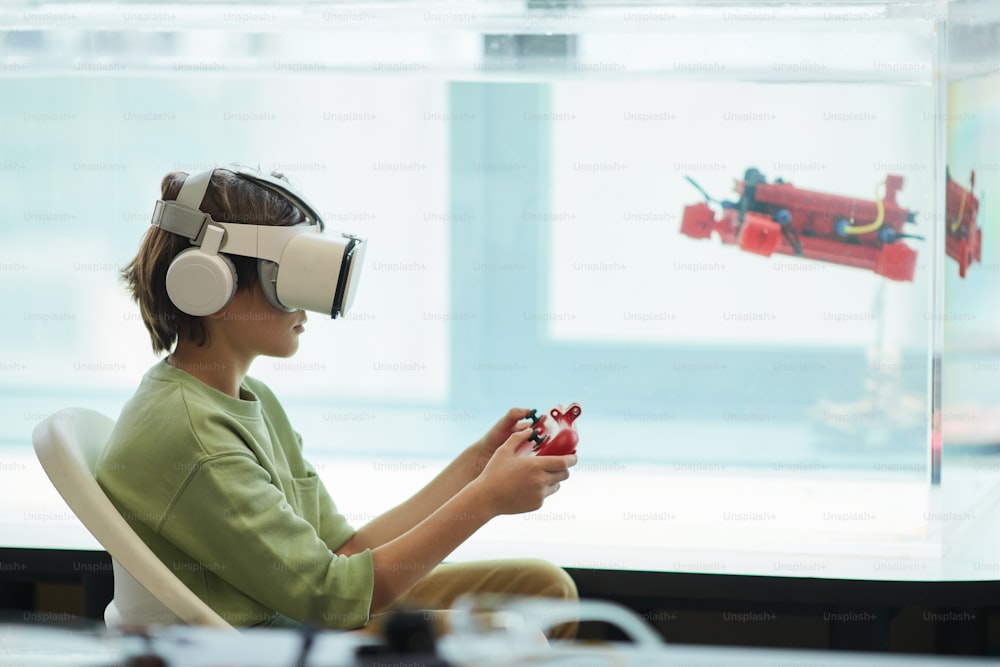 Retrato de vista lateral de un niño con auriculares VR mientras opera un bote robótico en el laboratorio de la escuela, espacio de copia