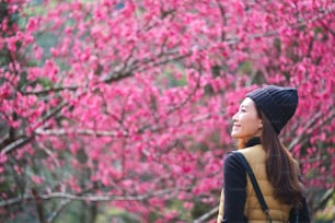 Porträtbild einer schönen jungen asiatischen Frau mit rosa Kirschblütenblume im Hintergrund