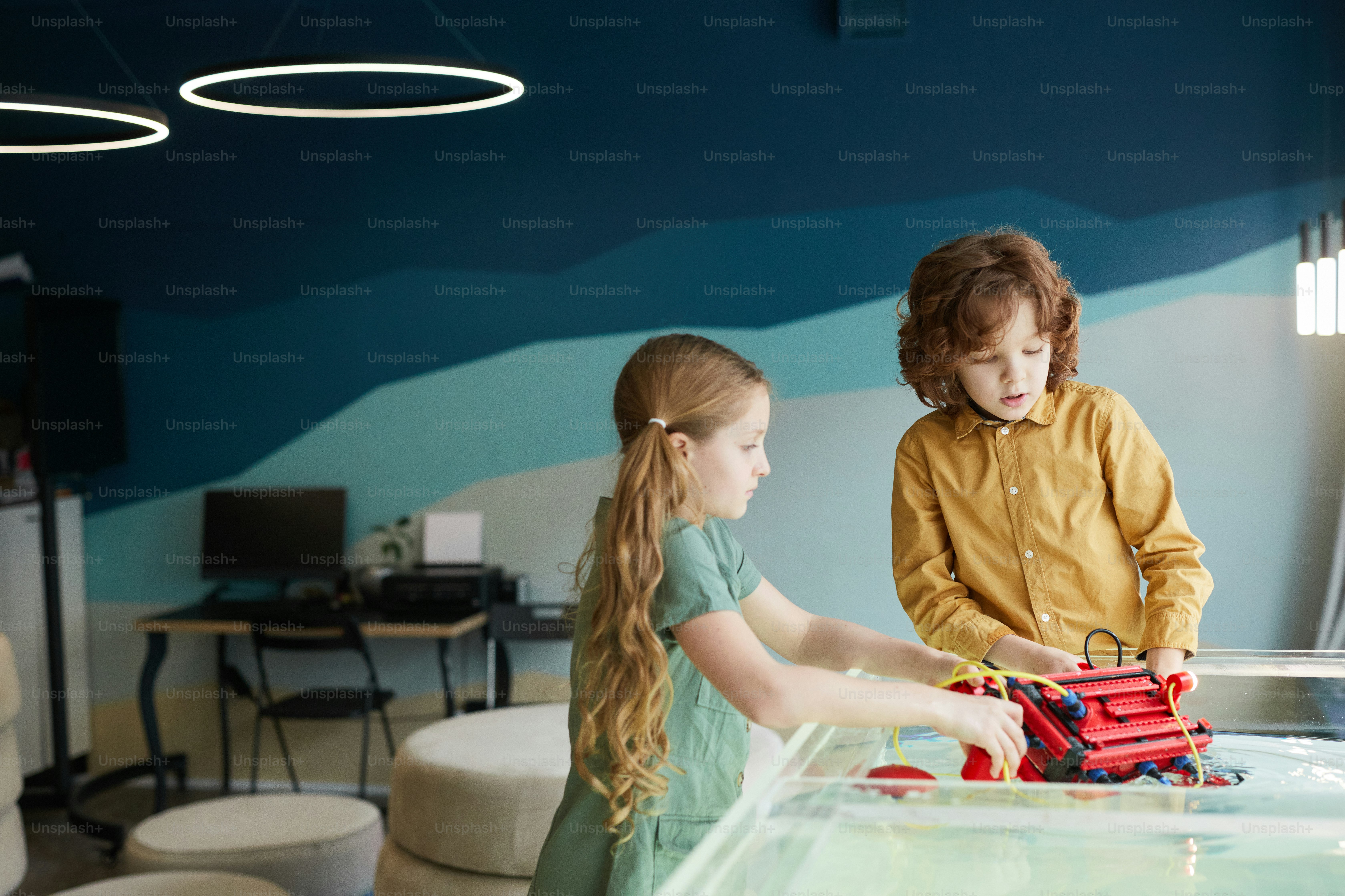 Portrait of two kids putting robo boat in water while experimenting with technology at robotics lab in school, copy space