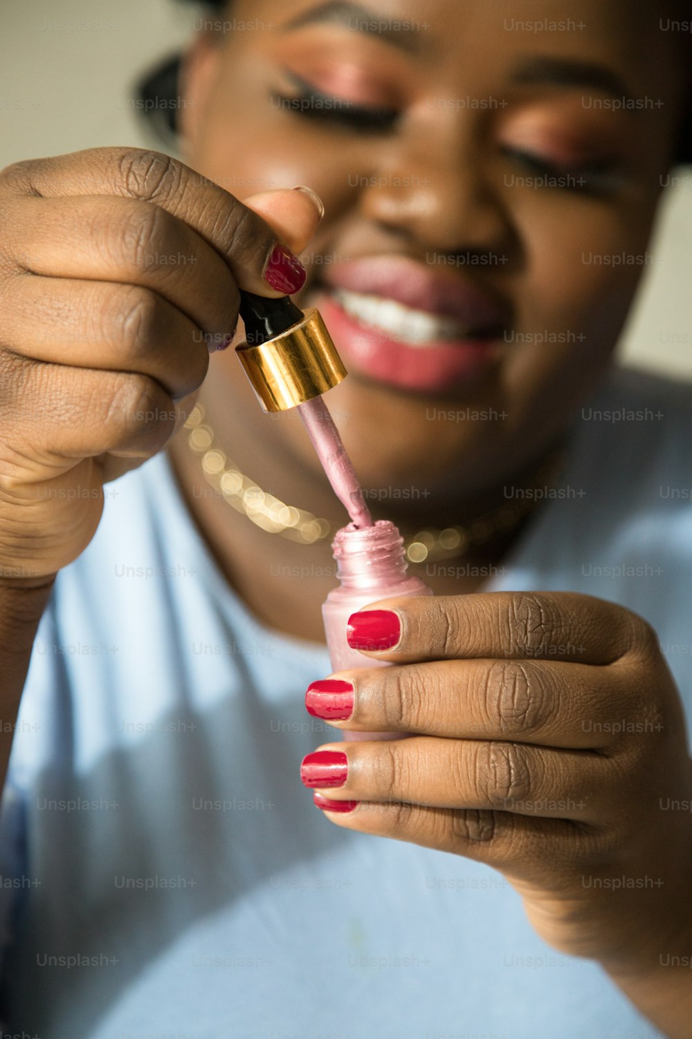 Portrait view of the attractive woman blogger with perfect skin holding nail polish and picks up it with a brush while beauty tutorial at home. Stock photo