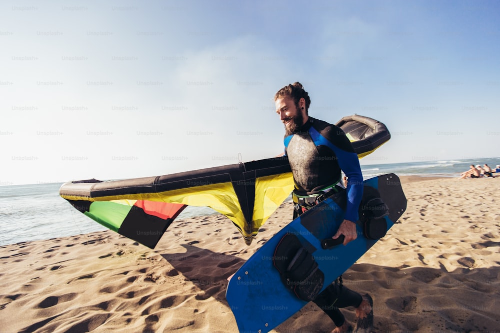 Junger Mann, professioneller Surfer, der mit seinem Kite am Sandstrand steht