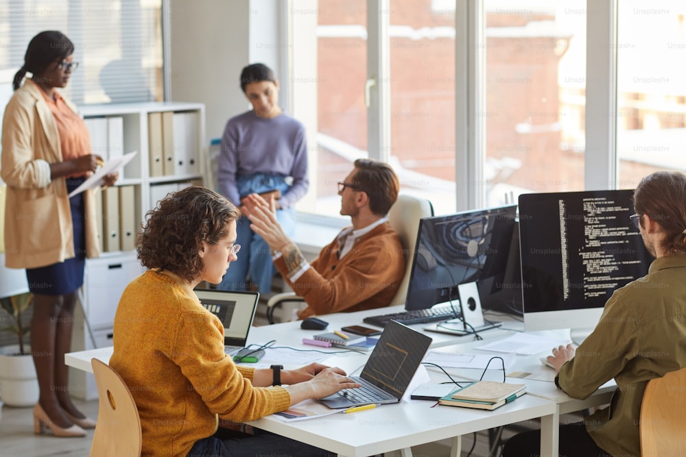 Diverse team of young software programmers using computers and writing code while collaborating on project in IT development studio, copy space