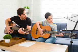 Enthusiastic music teacher playing the acoustic guitar together with a boy student learning the guitar chords of a beautiful song