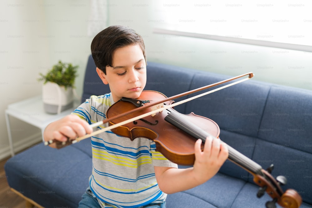 Ragazzo artistico che impara a suonare il violino con un arco e pratica le sue lezioni di musica. Bambino di talento che suona uno strumento musicale a casa