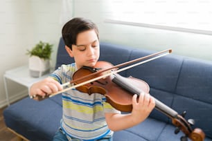 Menino artístico aprendendo a tocar violino com um arco e praticando suas aulas de música. Garoto talentoso tocando um instrumento musical em casa