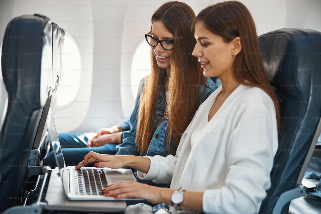 Friendly female passengers of an aircraft smiling while looking at the laptop screen during the flight