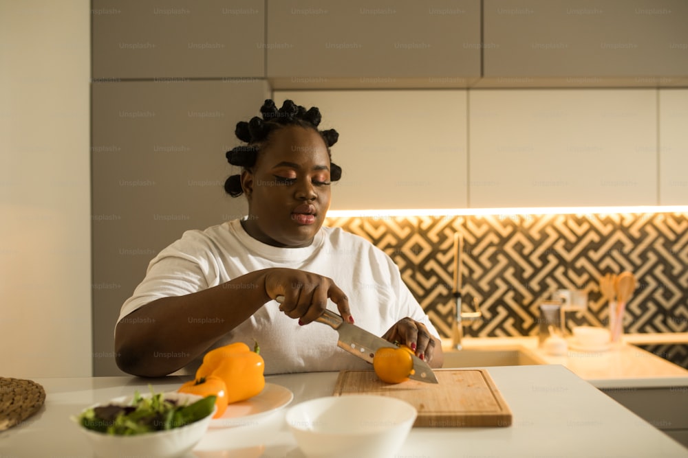 Beautiful multiracial woman is cutting ingredients on table while preparing vegetable salad in the kitchen. Healthy food, cooking at home and dieting concept