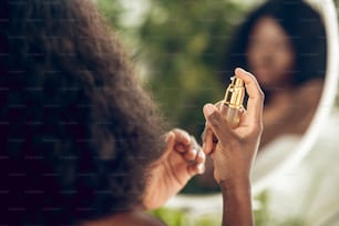 Haarpflege. Ansprechende afroamerikanische Frau, die Serum auf ihr Haar sprüht