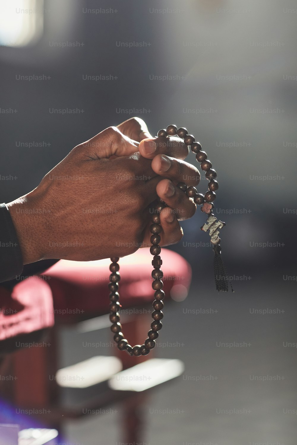 Primer plano de un hombre sosteniendo cuentas de rosario rezando mientras visita la iglesia