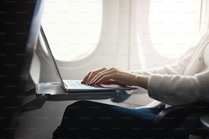 Beschnittenes Foto eines modernen Laptops und Hände einer Frau, die im Flugzeug auf einer Tastatur tippt