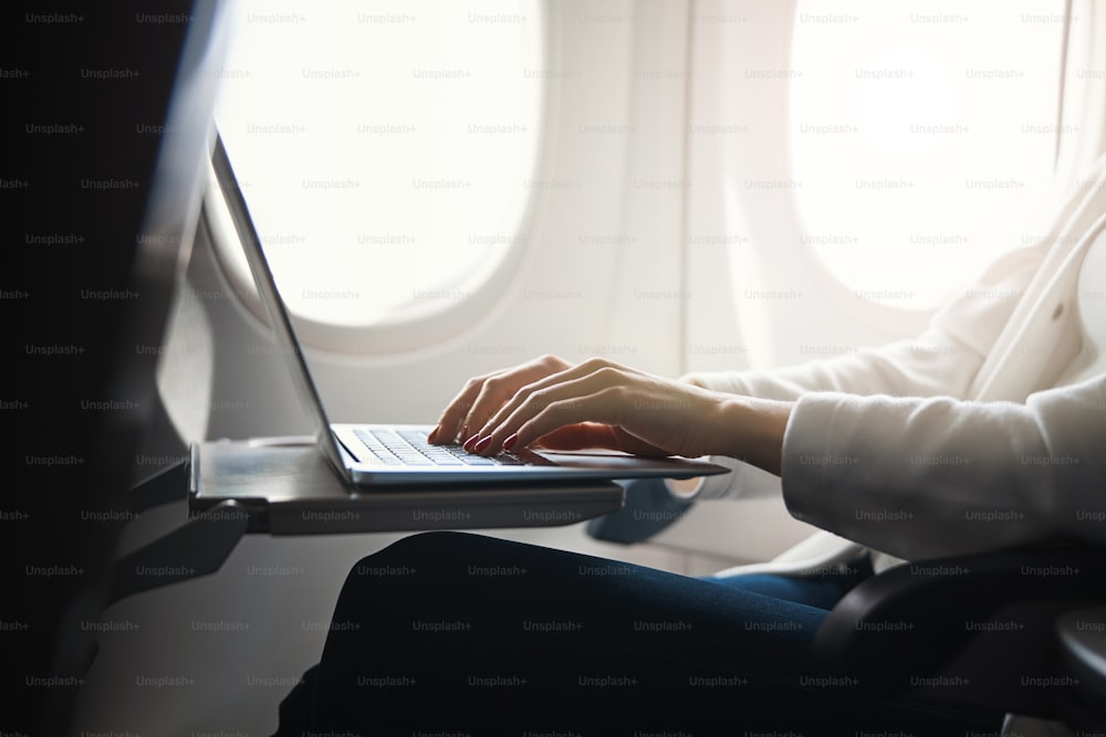 Foto recortada de una computadora portátil moderna y las manos de una mujer escribiendo en un teclado en el avión