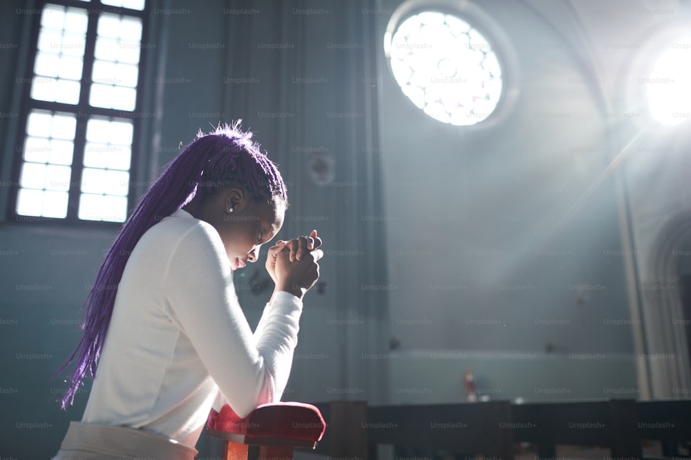 African young woman sitting in front of the altar in the church and praying