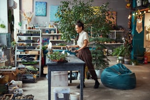 Side view of a cheerful professional florist filling a polyhedron terrarium container with potting mix