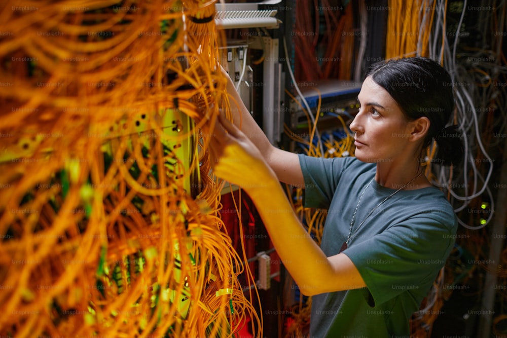 Side view portrait of young woman wearing military uniform inspecting server while working in server room, copy space