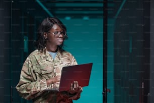 서버실에 서 있는 동안 �노트북을 사용하여 군복을 입은 젊은 아프리카계 미국인 여성의 허리 위로 초상화, 복사 공간