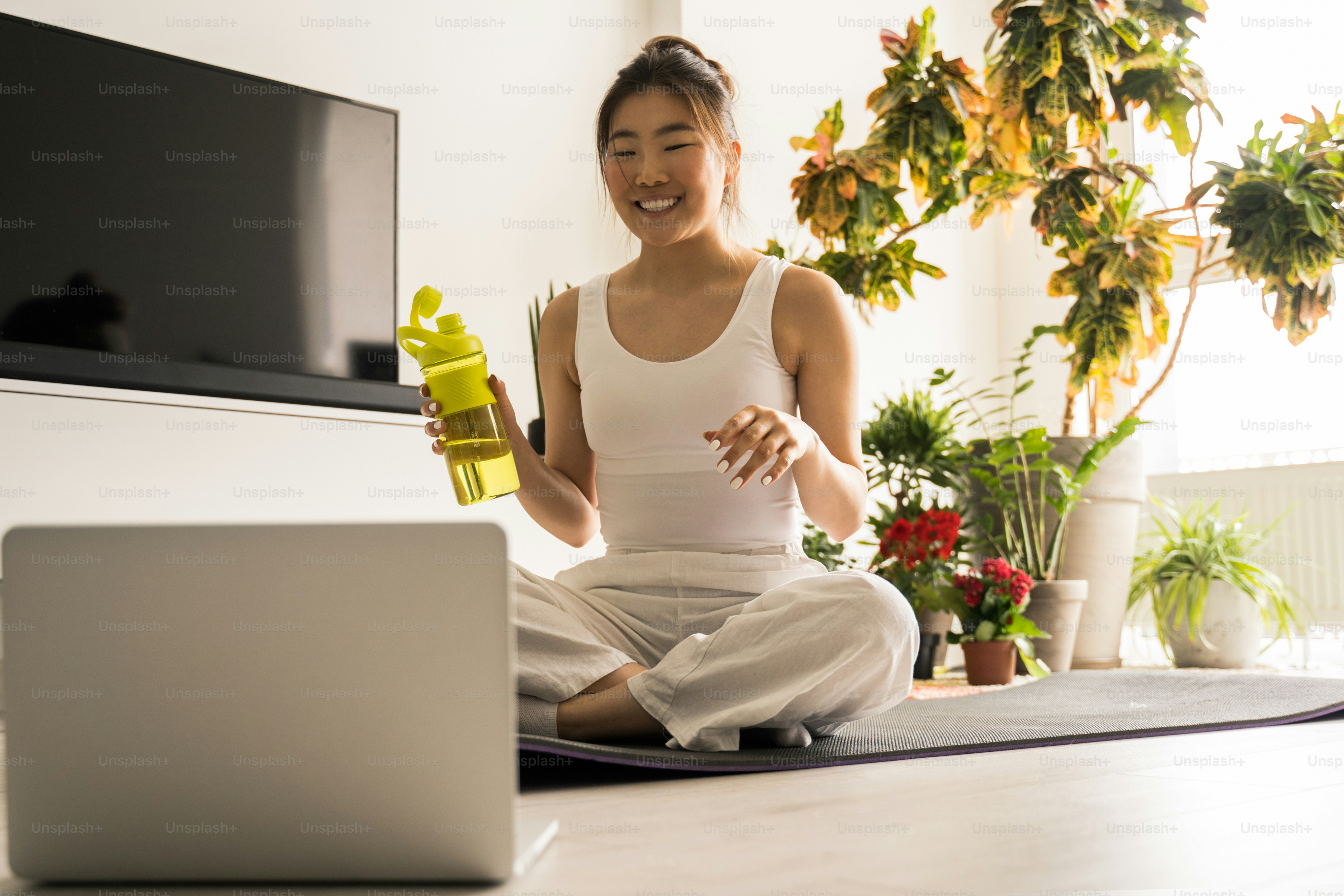 A woman in white activewear holding a yellow water bottle before a laptop