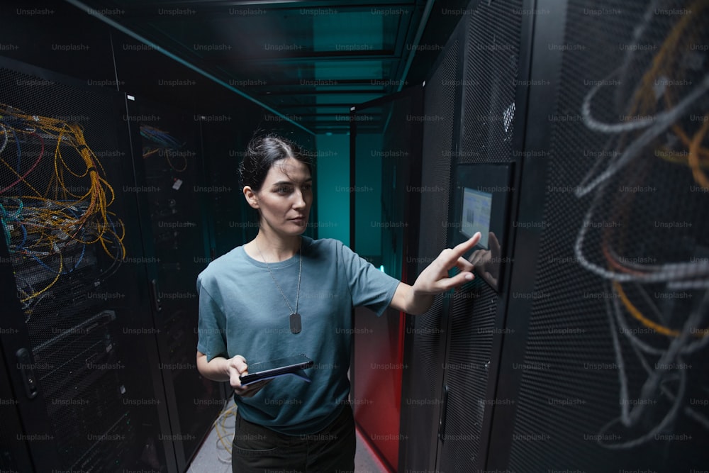 Retrato de cintura hacia arriba de una mujer militar usando el panel de control mientras configura servidores en el centro de datos, copie espacio