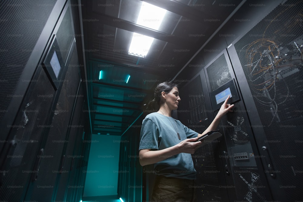 Low angle portrait of military woman using control panel while setting up servers in data center, copy space