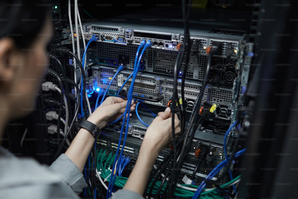 Primo piano del tecnico di rete femminile che collega i cavi nell'armadio del server durante l'installazione del supercomputer nel data center, spazio di copia