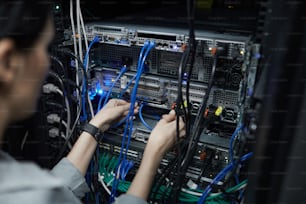 Gros plan d’une technicienne réseau féminine connectant des câbles dans une armoire de serveur lors de la configuration d’un supercalculateur dans un centre de données, espace de copie