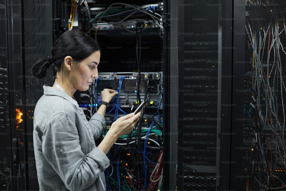 Vista lateral retrato da técnica de rede feminina conectando cabos no gabinete do servidor enquanto configura o supercomputador no data center, espaço de cópia