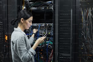 Vista laterale ritratto di un tecnico di rete femminile che collega i cavi nell'armadio del server durante la configurazione del supercomputer nel data center, spazio di copia